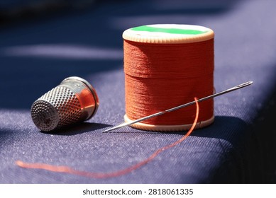 vibrant orange thread with a needle and thimble on dark blue fabric