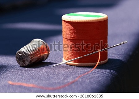 vibrant orange thread with a needle and thimble on dark blue fabric