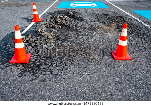 Vibrant orange and white traffic cones encircle
damaged surface of asphalt road. Bus parking lane sign painted in
blue and white.
