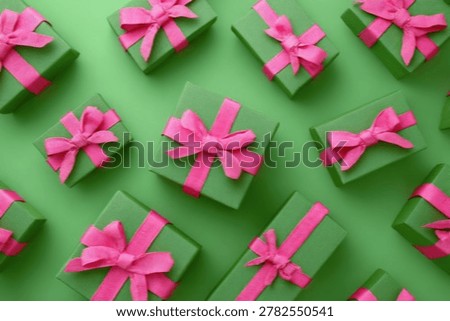 A vibrant overhead view of multiple green gift boxes, each adorned with a cheerful pink ribbon, artfully arranged on a plain green surface.
