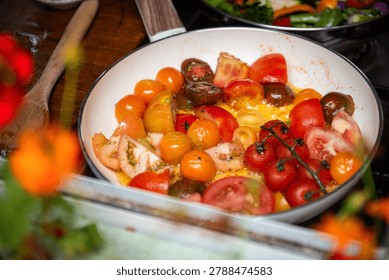 A vibrant pan of assorted cherry tomatoes being sauteed, showcasing a mix of red, yellow, and orange hues, with a wooden spoon nearby.