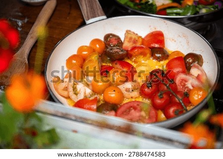 A vibrant pan of assorted cherry tomatoes being sauteed, showcasing a mix of red, yellow, and orange hues, with a wooden spoon nearby.