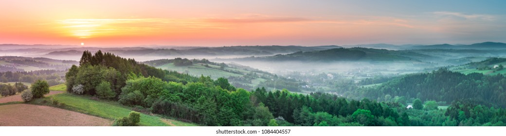 Vibrant panoramic sunrise over countryside hills in Poland. Spring mist and green fields.