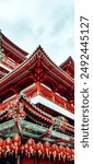 A vibrant photo of the Buddha Tooth Relic Temple in Singapore, showcasing its intricate red architecture and festive lanterns. The contrast against the cloudy sky highlights the cultural heritage.