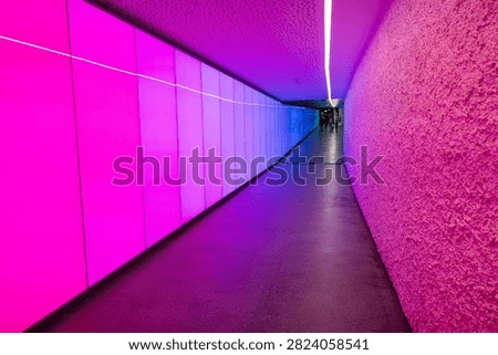 Vibrant pink and blue lighting transforms a curved modern underground pedestrian passage.