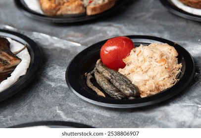 A vibrant plate of colorful vegetable medley including pickled greens, a juicy tomato, and shredded cabbage served artfully on a black dish in a rustic dining setting - Powered by Shutterstock