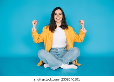 Vibrant Portrait of a Joyful Girl Celebrating Success with Raised Fists and a Victorious 'Yes ' - Isolated on Blue Background - Positive, Optimistic Emotions - Powered by Shutterstock