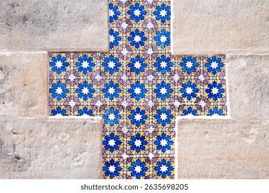 Vibrant Portuguese azulejo tiles form a striking cross pattern embedded in a weathered stone wall. A blend of history, artistry, and texture.