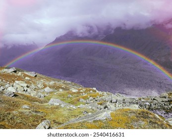 A vibrant rainbow arcs over misty mountains, partially obscured by soft fog. Below, a lush green valley basks in gentle sunlight, creating a serene atmosphere. The scene radiates a dreamy, enchanting  - Powered by Shutterstock