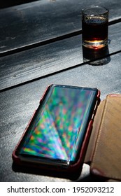 Vibrant Rainbow Rays Reflect In Mobile Phone Screen On Black Table With Alcohol Drink Shot Glass. Defocused Multicolored Beams And Reflection In Smartphone Screen Surface