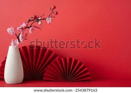 A vibrant red backdrop featuring a white vase with cherry blossom branches, complemented by red paper fans. Perfect for celebrating the Chinese New Year 2025 with cultural elegance