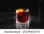 A vibrant red cocktail in a short glass, garnished with an orange slice, set against a dark background. Perfect for themes of nightlife, beverages, and celebrations. Ideal for stock photography use.