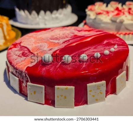 A vibrant red mirror-glaze mousse cake decorated with glossy white pearls and geometric chocolate tiles, presented on a clean white board for a striking commercial look.