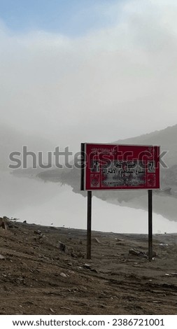 A vibrant red sign with the warning 'no swimming'  in Arabic on a slope of a hill
