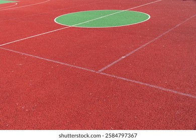 The vibrant red sporting surface features large green circles, ideal for various outdoor activities under clear blue skies.