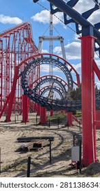 A vibrant roller coaster track intertwines against a blue sky, showcasing an amusement park's thrill rides under construction.