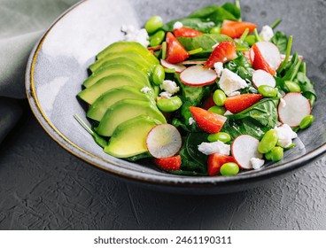 Vibrant salad with spinach, avocado, strawberries, and feta cheese served on a modern plate