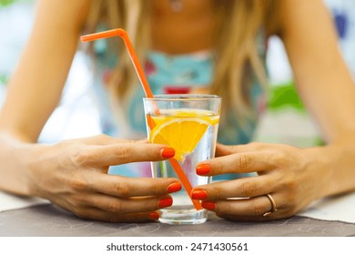 A vibrant scene capturing a woman savoring a chilled drink with a slice of orange, highlighting a moment of refreshment.