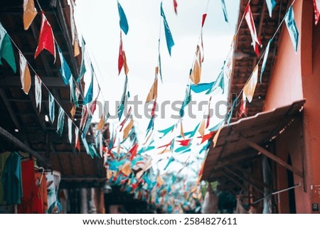 A vibrant scene featuring colorful triangular flags strung across a lively marketplace. The flags, in shades of red, blue, yellow, and green, flutter against a bright sky, adding a festive atmosphere 