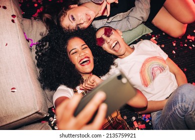 Vibrant selfies for vibrant people. Overhead view of three happy friends taking a selfie while lying on the floor at a house party. Group of cheerful female friends having fun together on the weekend. - Shutterstock ID 2135759921
