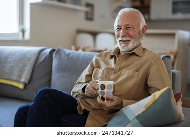 Vibrant senior Caucasian man relaxing at home. He is sitting on the sofa in his living room drinking hot tea. Retirement, independence, and simple pleasures concepts. - Powered by Shutterstock