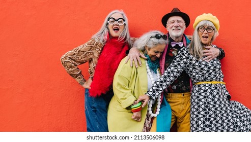 Vibrant senior citizens having a good time while standing together against a red background. Group of cheerful elderly friends celebrating their retirement in colourful clothing. - Powered by Shutterstock