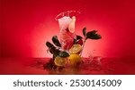 A vibrant splash surrounds a pink drink, garnished with citrus slices, fresh green leaves, and berries, set against a bold red background.