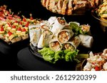 A vibrant spread of wraps filled with vegetables and chicken, tied with string and garnished with lettuce on a decorative platter at event catering