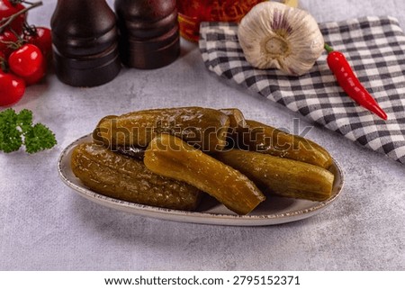 Vibrant still life composition features plate of briny pickled cucumbers. Fresh red cherry tomatoes, garlic bulb, hot chili pepper, green parsley sprigs arranged on textured grey background