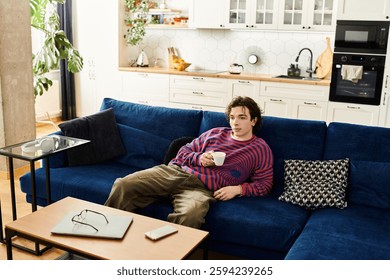 In a vibrant striped sweatshirt, a young non binary person enjoys coffee while lounging at home.