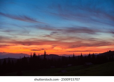 Vibrant sunset fills sky with brilliant shades of orange, pink, and purple, casting warm glow over landscape. Tall pine trees stand in silhouette against colorful horizon, with rolling hills. - Powered by Shutterstock