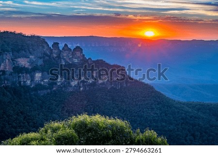 A vibrant sunset illuminates the iconic Three Sisters rock formation in the Blue Mountains National Park of Australia.