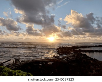 A vibrant sunset illuminates the ocean as colorful clouds drift across the sky, casting a warm glow over the calm waves and rocky shoreline at Lydgate Beach Park. - Powered by Shutterstock