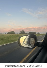 A vibrant sunset is reflected in the side mirror of a car, with a phone held up capturing the view.
