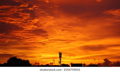 A vibrant sunset with shades of orange, pink, and purple lighting up the sky, silhouetting trees and rooftops, creating a serene and warm atmosphere. - Powered by Shutterstock