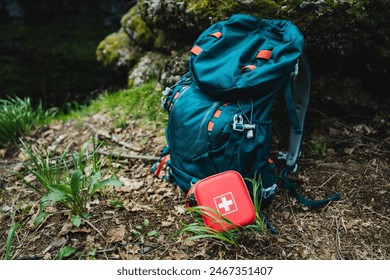 A vibrant teal backpack and red first aid kit on a forest floor highlight the importance of outdoor adventure preparedness. Essential gear for hiking, camping, and exploration in the wilderness - Powered by Shutterstock