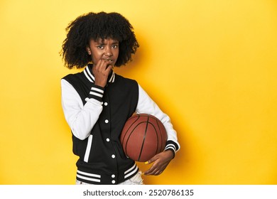 Vibrant teen girl with basketball on yellow studio background biting fingernails, nervous and very anxious. - Powered by Shutterstock