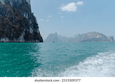 The vibrant turquoise waters of Phang Nga Bay reflect the clear blue sky, framed by towering limestone cliffs, creating a tranquil coastal paradise under the sun. - Powered by Shutterstock