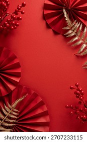 Vibrant vertical red backdrop with round paper fans, red berries, and gold fern sprigs, embodying Chinese New Year spirit with festive charm ideal for greeting cards and seasonal promotions