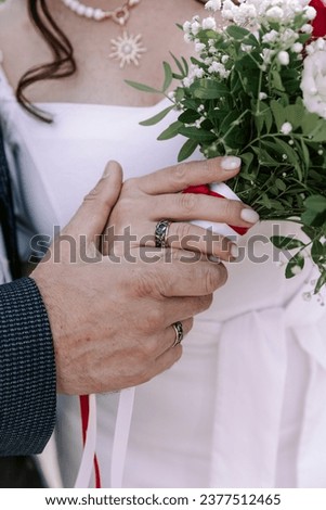 A vibrant vertical wedding photograph capturing a close-up of the bride and groom's hands, showcasing their wedding rings. In the background, a close-up of the bride and groom, as well as the bridal b