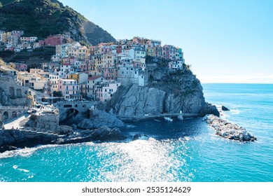 A vibrant village clings to a cliff along the stunning Cinque Terre coastline, with pastel-colored houses rising above the azure sea. Manarola in Cinque Terre Italy - Powered by Shutterstock