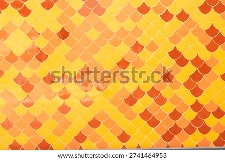 A vibrant wall featuring fish scale ceramic tiles in a gradient of orange, yellow, and amber tones.