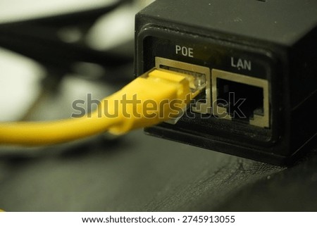 A vibrant yellow ethernet cable is shown plugged into the LAN port of a black Power over Ethernet adapter, illustrating an active network connection.