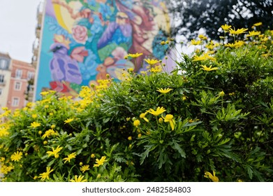 Vibrant yellow flowers bloom in the foreground, with a colorful mural decorating a building in lisbon in the background. - Powered by Shutterstock