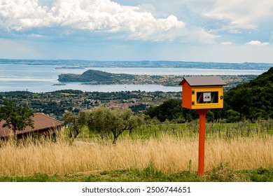 A vibrant yellow little free library stands on a hilltop overlooking a serene lake and picturesque countryside. The tranquil scene offers a perfect escape to nature, inviting readers to relax. - Powered by Shutterstock