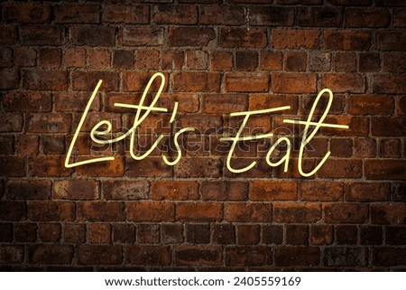 A Vibrant Yellow Neon Sign Saying Let's Eat In A Restaurant Or Cafe