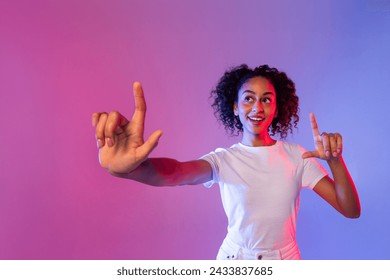 Vibrant young black woman with curly hair excitedly interacts with virtual touch screen, fingers extended, against dynamic pink and blue neon backdrop - Powered by Shutterstock