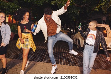 Vibrant Young Man Showing His Friends Some Dance Moves At Night. Group Of Happy Young People Walking Together While Holding Beer Cans. City Friends Having A Good Time On The Weekend.