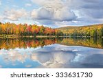 Vibrantly colorful fall foliage and white clouds in a blue sky are reflected on Lake Plumbago at Alberta in Upper Peninsula Michigan.