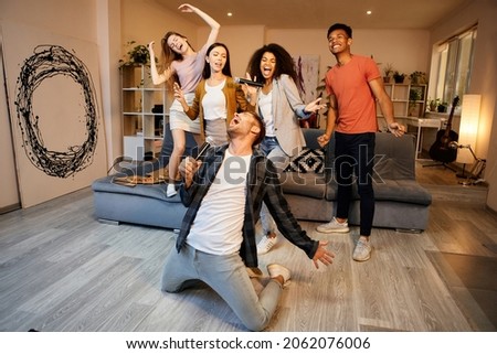 Vibrations for good fun. Full length shot of handsome young guy looking enthusiastic while singing with microphone, playing karaoke with friends in the modern apartment